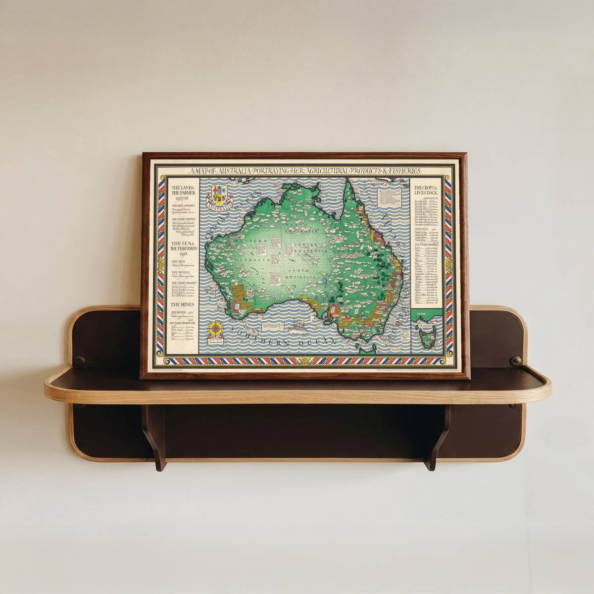 Framed art print of A Map of Australia Portraying Her Agricultural Products & Fisheries by MacDonald Gill, in a dark wood frame resting on a wall shelf