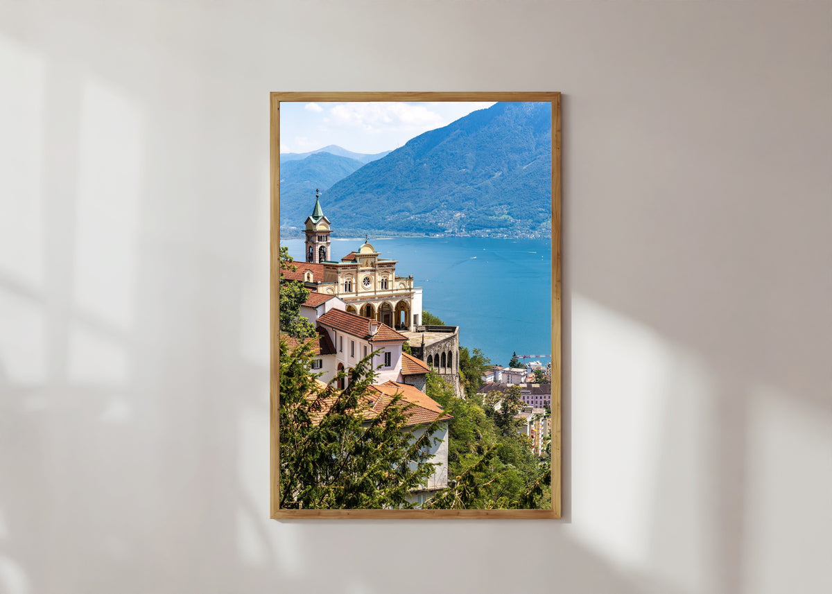 Framed art print of Madonna del Sasso in Orselina by Daniela Faust, in a light wood frame on a sunlit white wall