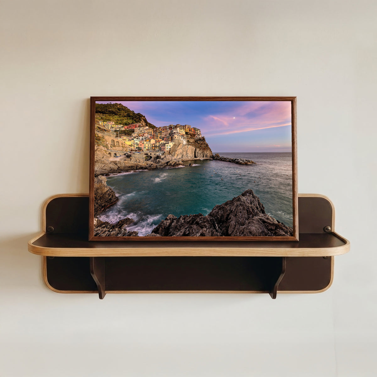 Framed art print of Manarola Sunset by Pablo Meilán Campagnale, in a dark wood frame resting on a wall shelf