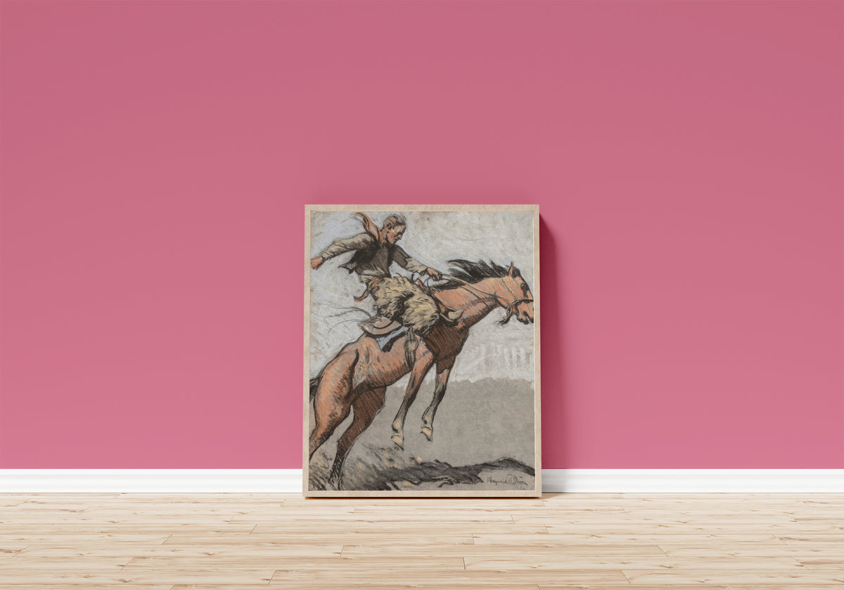 Framed art print of Bronco Buster by Maynard Dixon, in a light wood frame leaning on a pink wall above a wooden floor