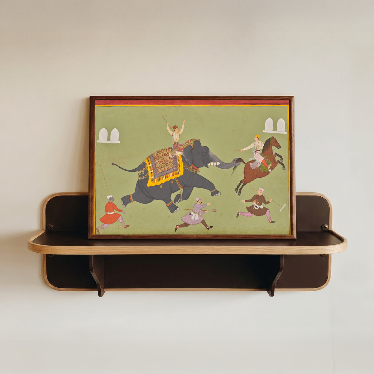 Framed art print of The Elephant of Maharana Jai Singh of Mewar Catches a Horse by the Tail by Mewar school, in a dark wood frame resting on a wall shelf