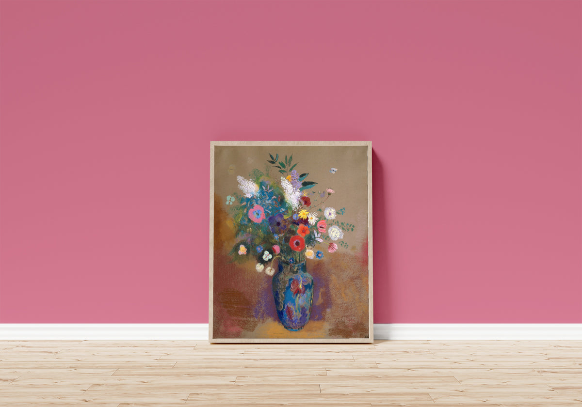 Framed art print of Bouquet of Flowers (Blue Vase) by Odilon Redon, in a light wood frame leaning on a pink wall above a wooden floor