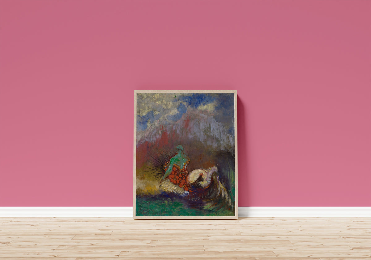 Framed art print of Siren by Odilon Redon, in a light wood frame leaning on a pink wall above a wooden floor