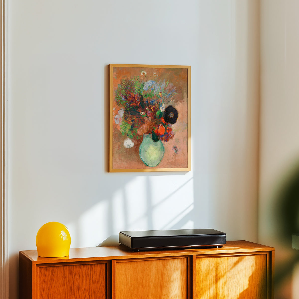 Framed art print of The Black Poppy by Odilon Redon, in a light wood frame on a white wall above an orange sideboard