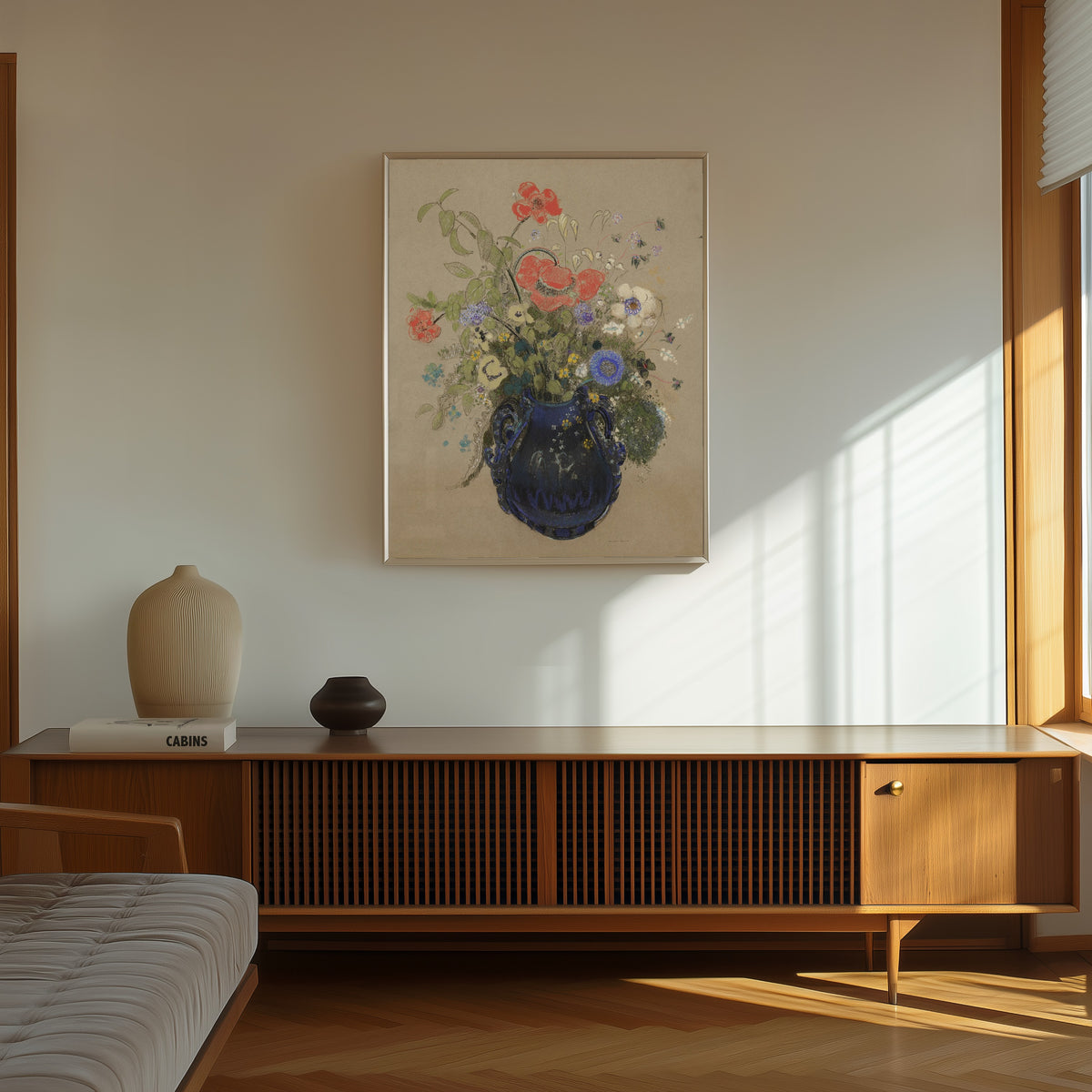 Framed art print of Vase of Flowers (Grey Background) by Odilon Redon, in a thin light frame on a sunlit wall above a wooden sideboard
