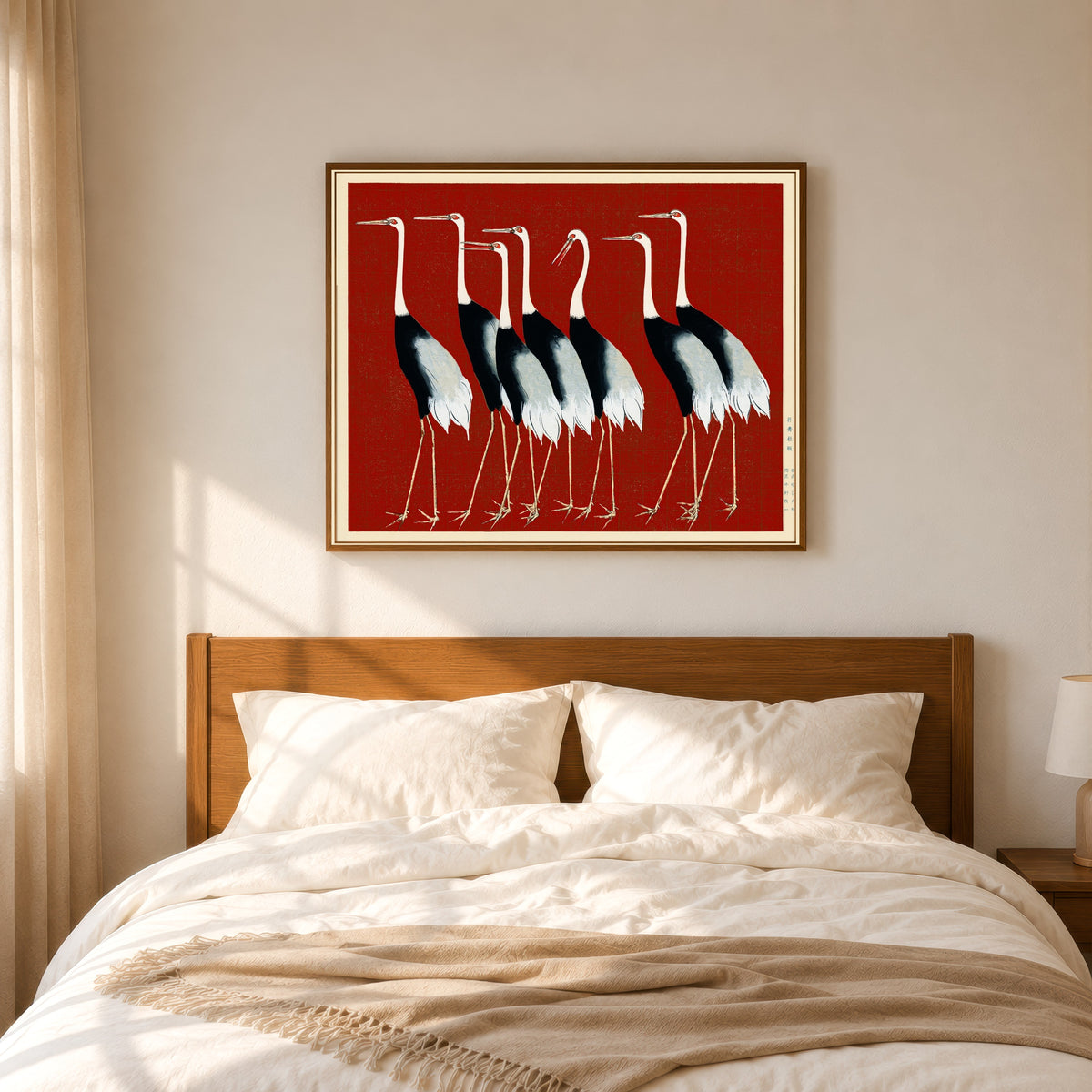 Framed art print of Cranes in Red by Ogata Korin, in a slim wood frame above a bed in a sunlit bedroom