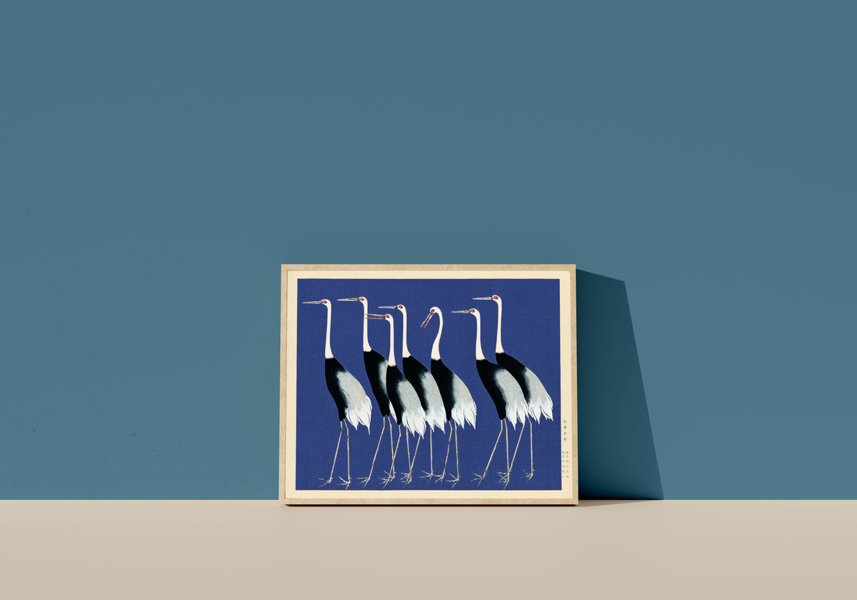 Framed art print of Cranes in Blue by Ogata Korin, in a light wood frame leaning on a blue wall