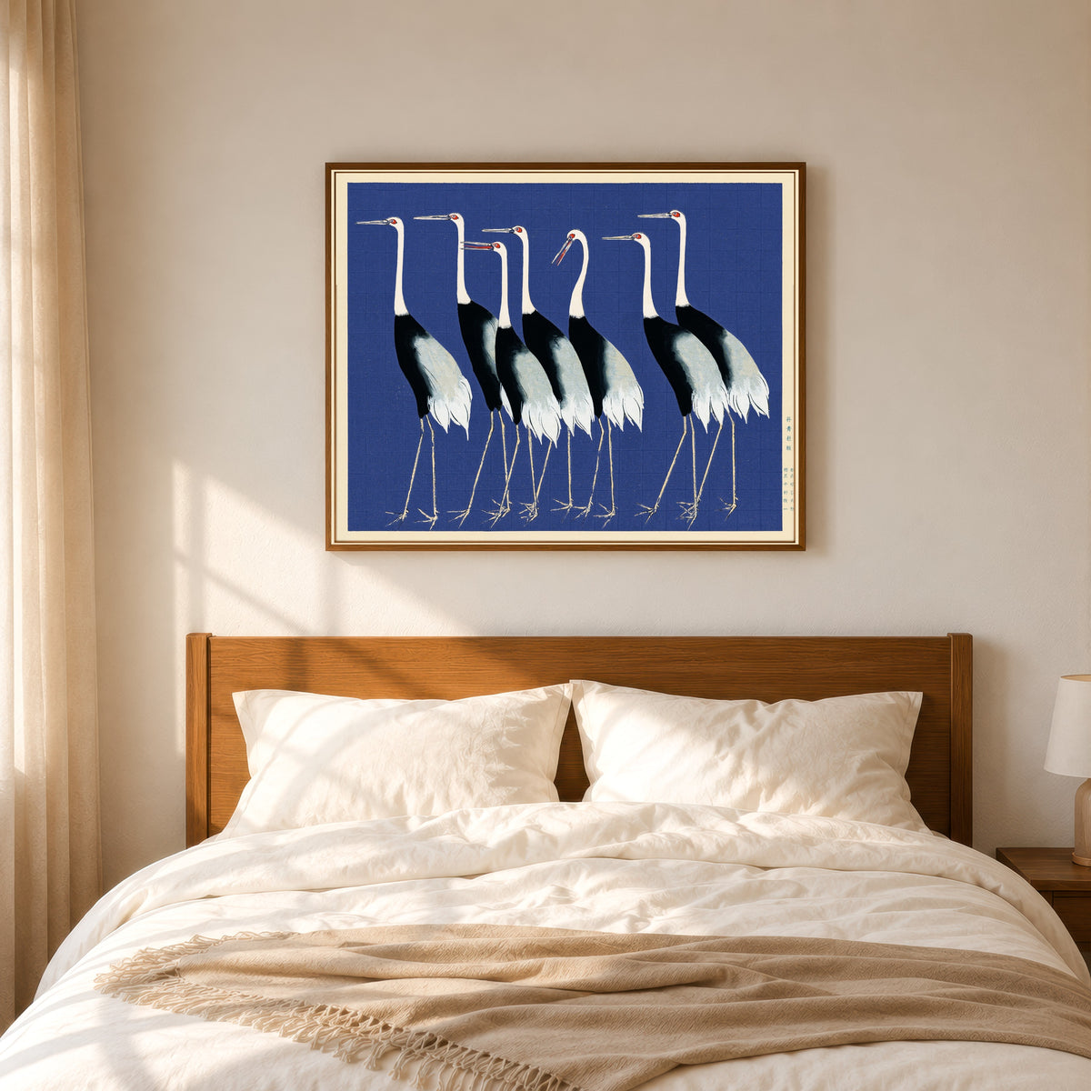 Framed art print of Cranes in Blue by Ogata Korin, in a slim wood frame above a bed in a sunlit bedroom