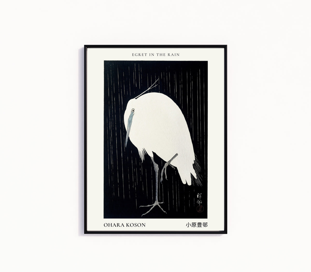 Framed art print of Egret in the Rain by Ohara Koson, in a slim black frame on a plain white wall