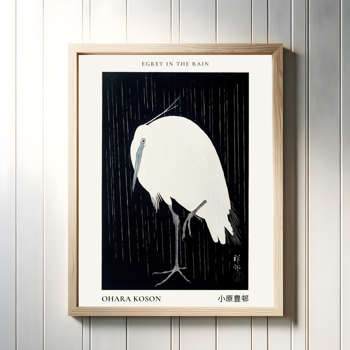 Framed art print of Egret in the Rain by Ohara Koson, in a light wood frame on a white panelled wall