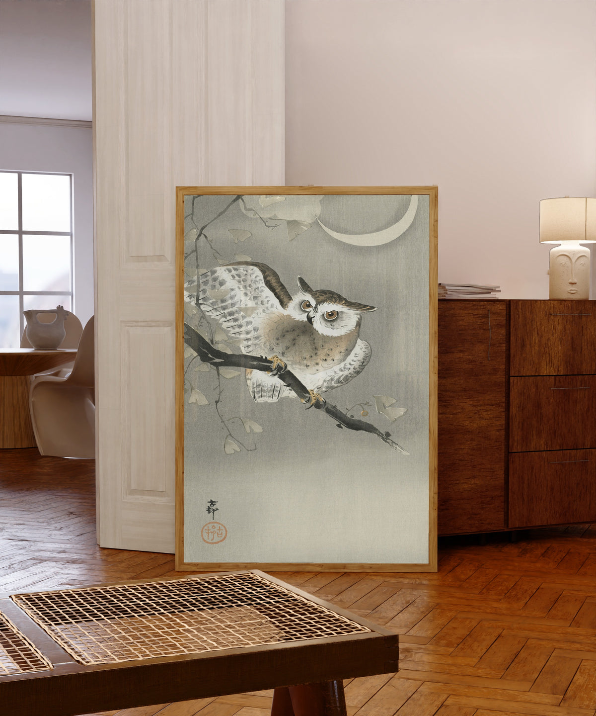 Framed art print of Long-eared Owl in Ginkgo by Ohara Koson, in a light wood frame leaning in a warm room with a parquet floor