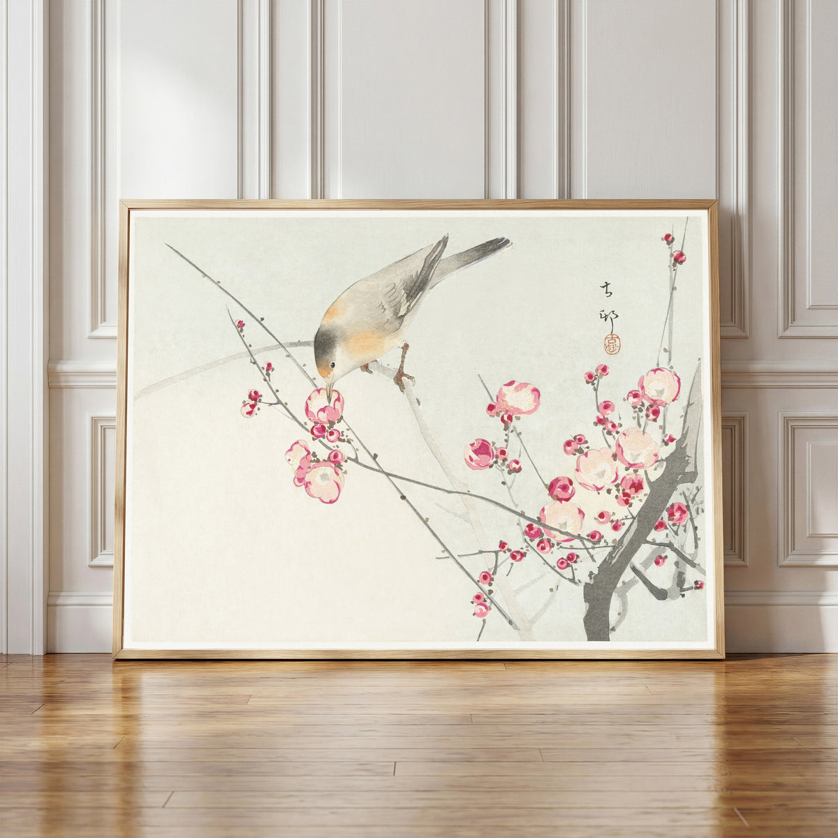 Framed art print of Songbird on Blossom Branch by Ohara Koson, in a light wood frame leaning against a panelled white wall