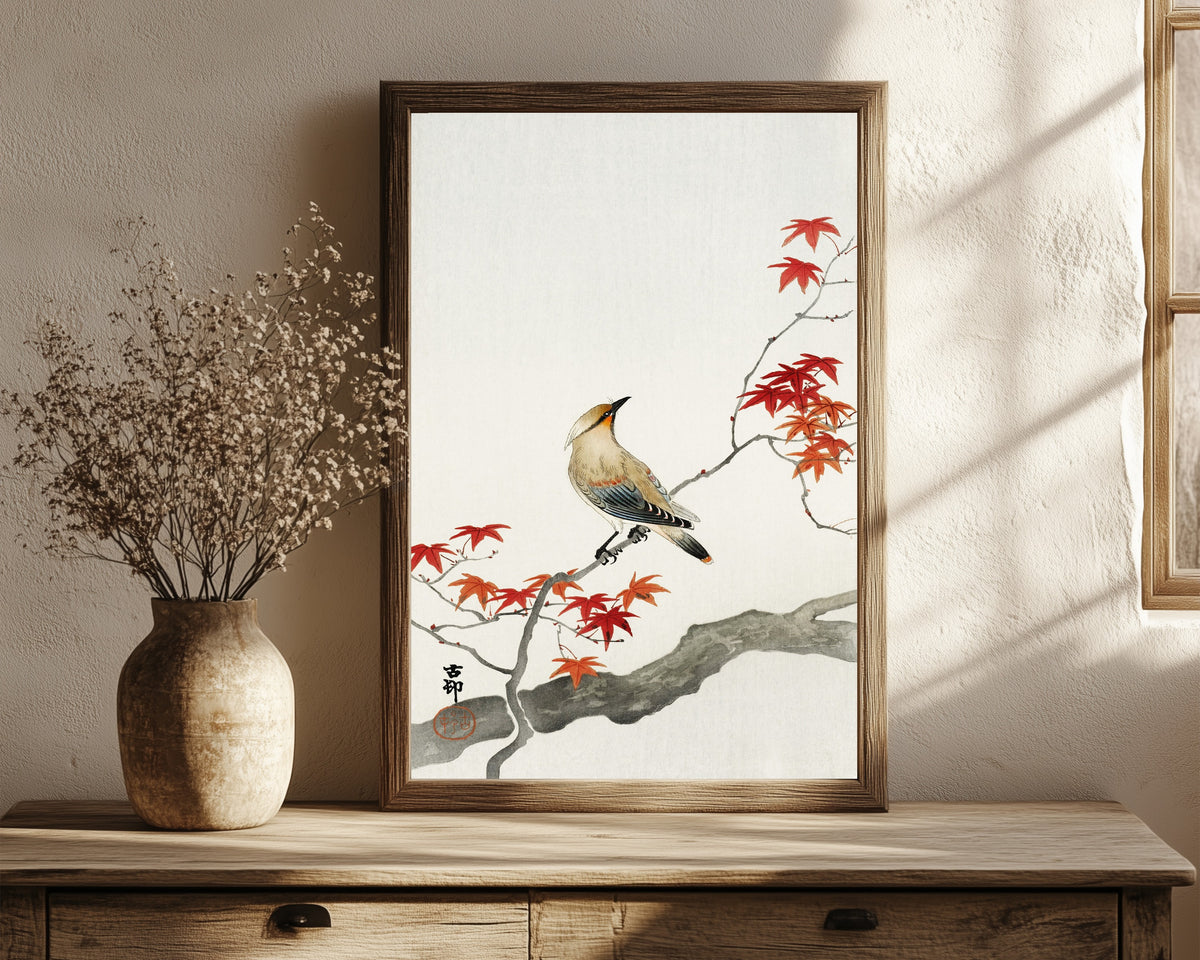 Framed art print of Waxwing on Maple by Ohara Koson, in a dark wood frame leaning on a rustic console beside dried flowers