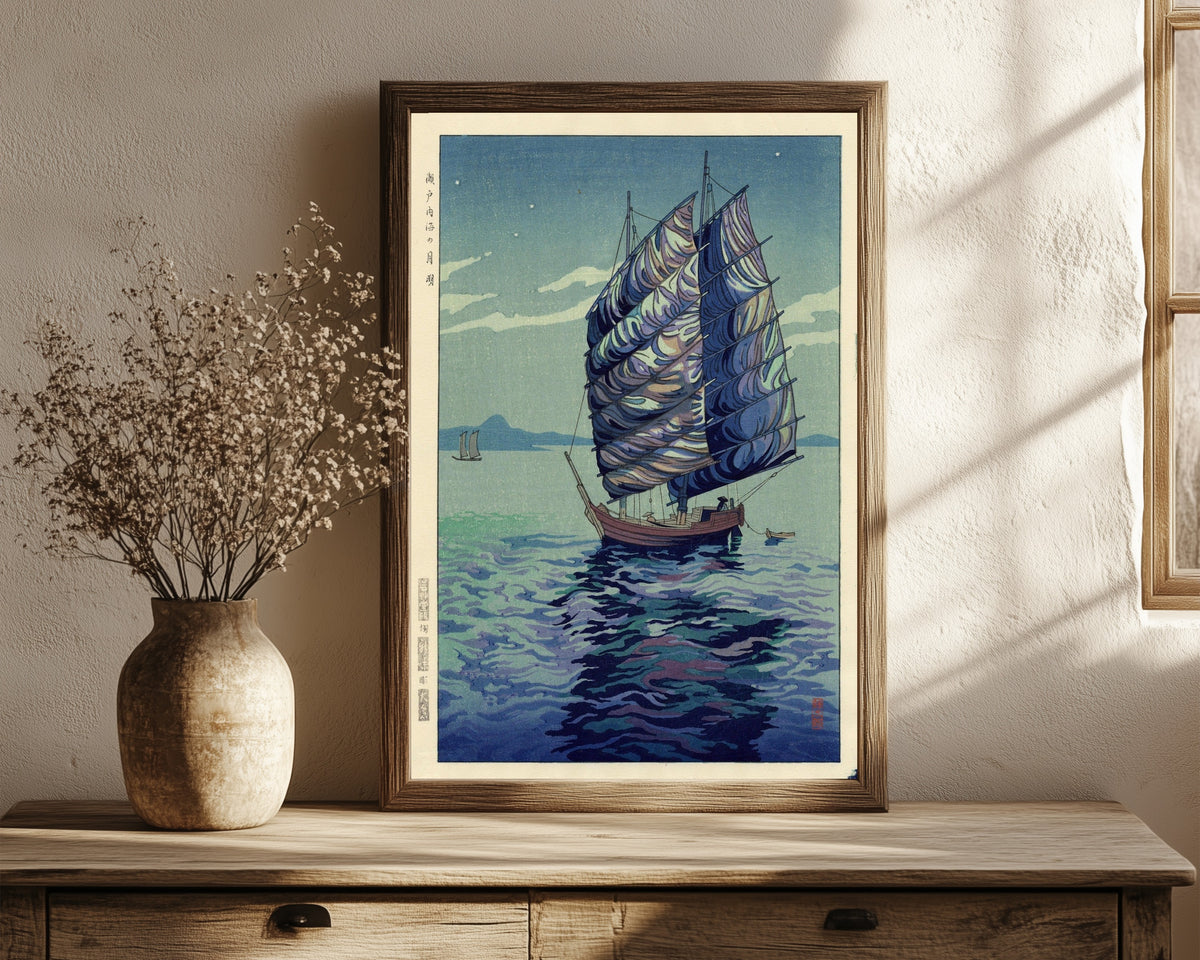 Framed art print of Moonlight Over Inland Sea by Okazaki Shintaro, in a dark wood frame leaning on a rustic console beside dried flowers