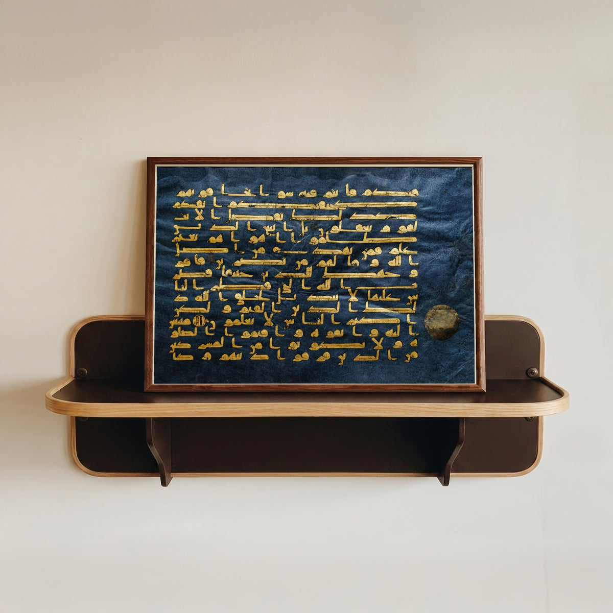 Framed art print of Ancient Islamic Calligraphy Art Print by The Blue Qur'an, in a dark wood frame resting on a wall shelf