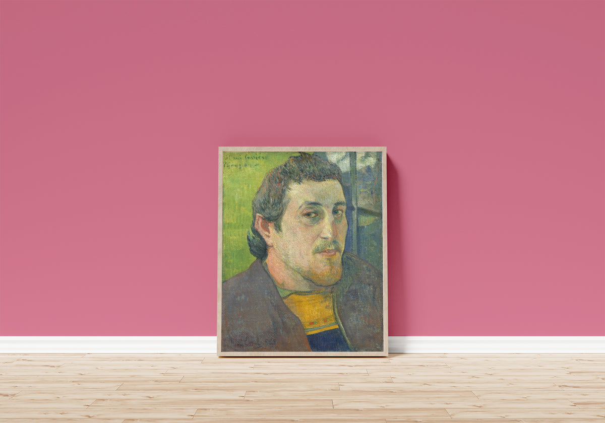 Framed art print of Self-Portrait Dedicated to Carrière by Paul Gauguin, in a light wood frame leaning on a pink wall above a wooden floor