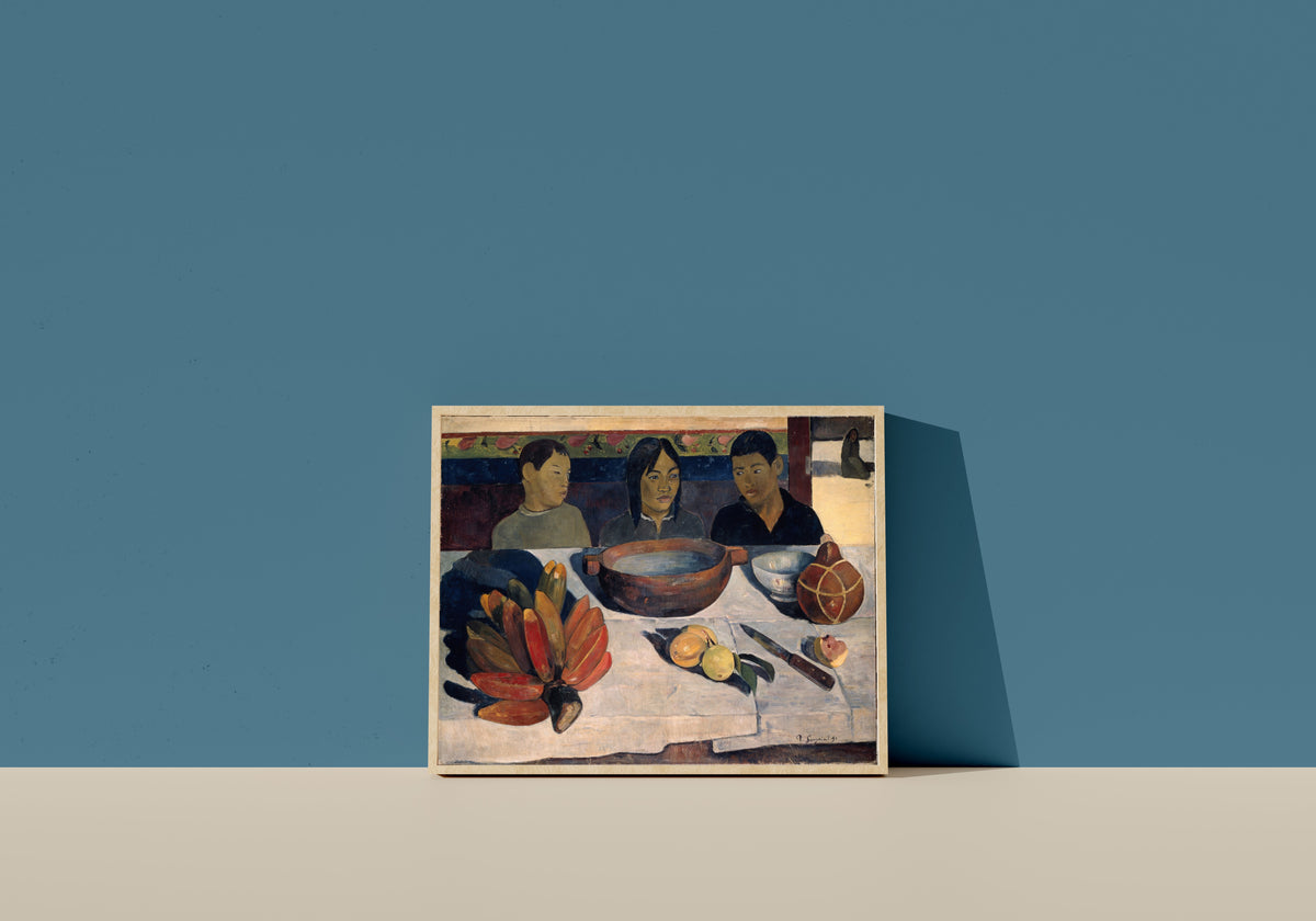 Framed art print of The Meal (Bananas) by Paul Gauguin, in a light wood frame leaning on a blue wall