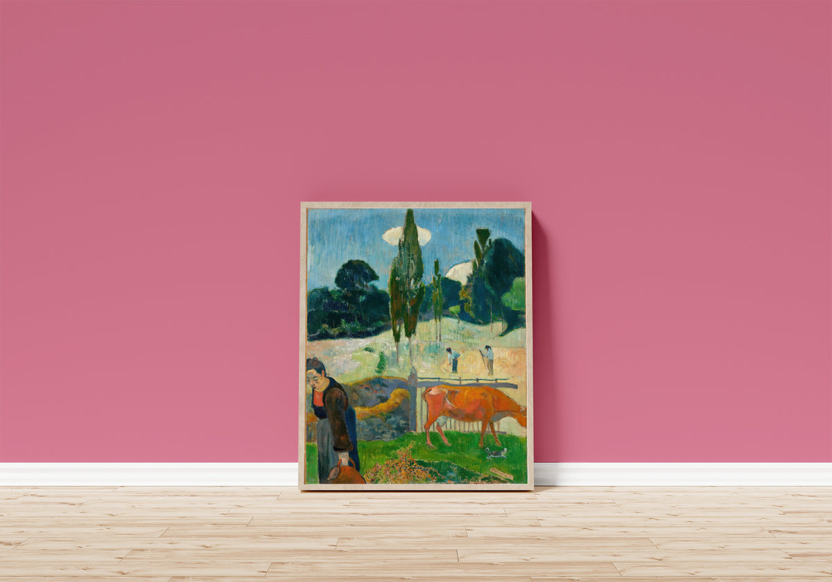 Framed art print of The Red Cow by Paul Gauguin, in a light wood frame leaning on a pink wall above a wooden floor