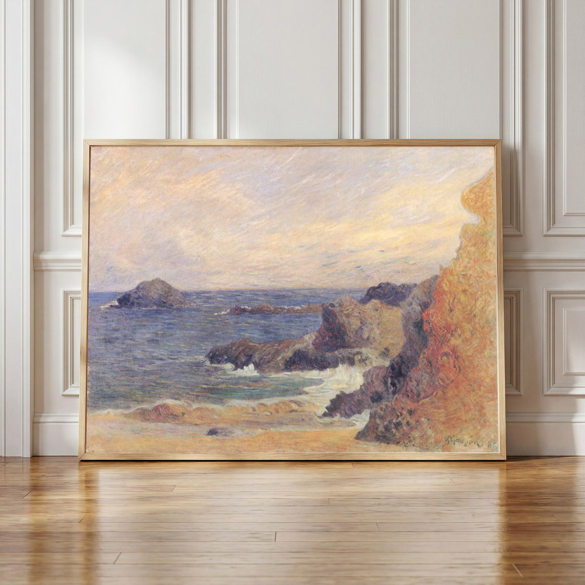 Framed art print of The Rocky Coast (Rocks by the Sea) by Paul Gauguin, in a light wood frame leaning against a panelled white wall