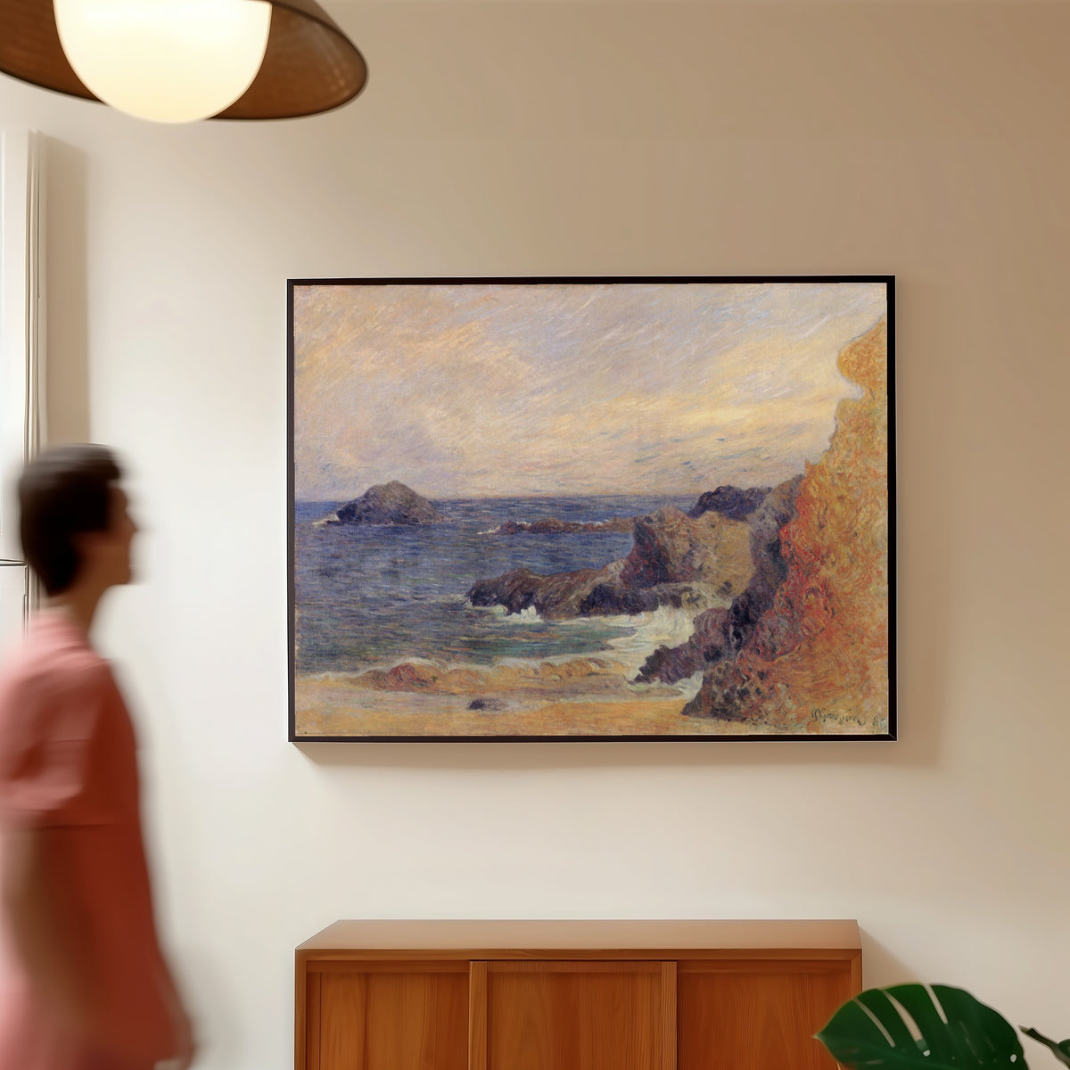 Framed art print of The Rocky Coast (Rocks by the Sea) by Paul Gauguin, in a slim black frame on a warm wall in a sunlit room