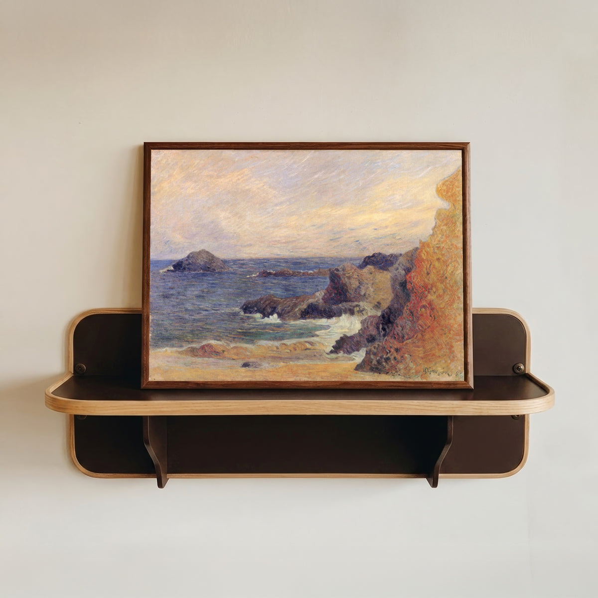 Framed art print of The Rocky Coast (Rocks by the Sea) by Paul Gauguin, in a dark wood frame resting on a wall shelf