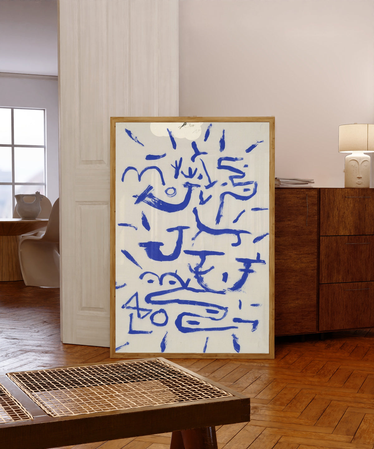 Framed art print of Creeper and Climber by Paul Klee, in a light wood frame leaning in a warm room with a parquet floor
