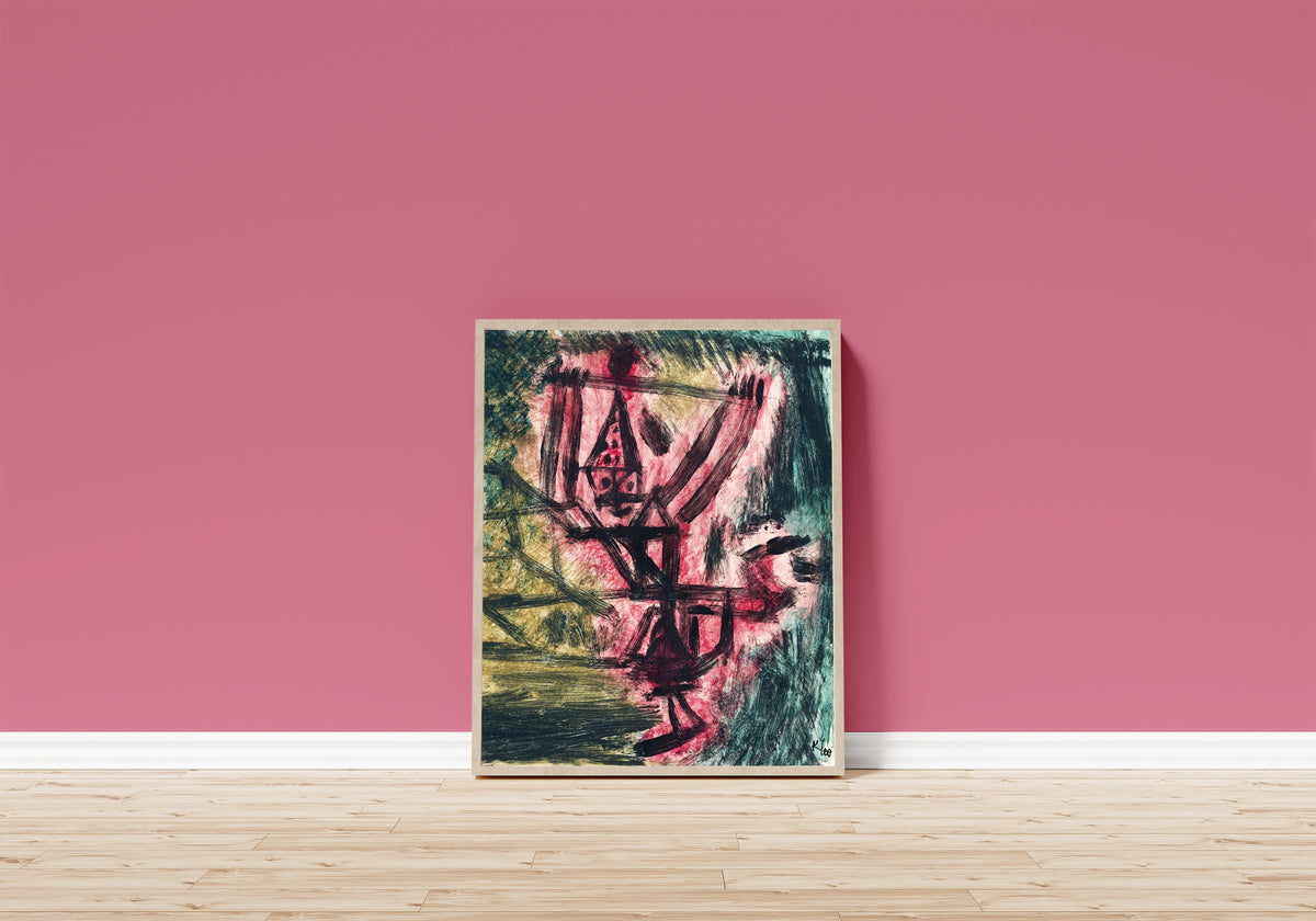 Framed art print of Fire Clown by Paul Klee, in a light wood frame leaning on a pink wall above a wooden floor