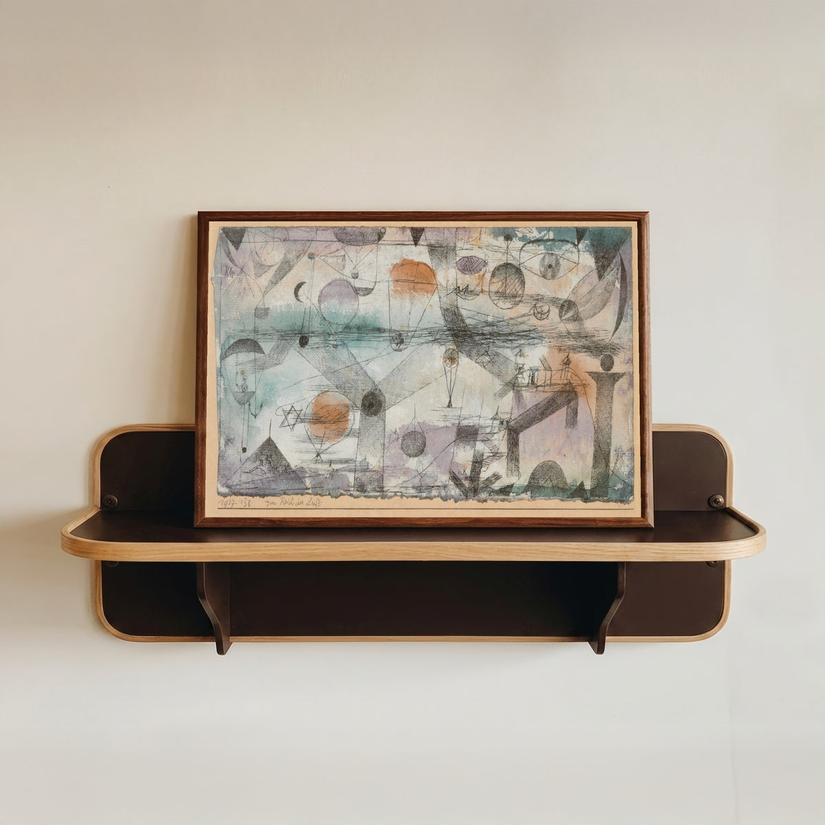 Framed art print of In the Realm of Air (Im Reich der Luft) by Paul Klee, in a dark wood frame resting on a wall shelf