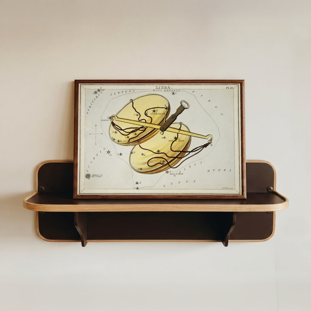 Framed art print of Libra by Sidney Hall, in a dark wood frame resting on a wall shelf