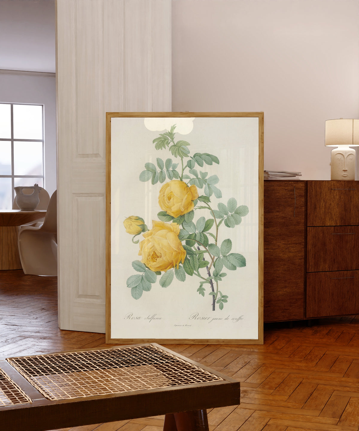 Framed art print of Les Roses: Rosa Sulfurea by Pierre-Joseph Redouté, in a light wood frame leaning in a warm room with a parquet floor