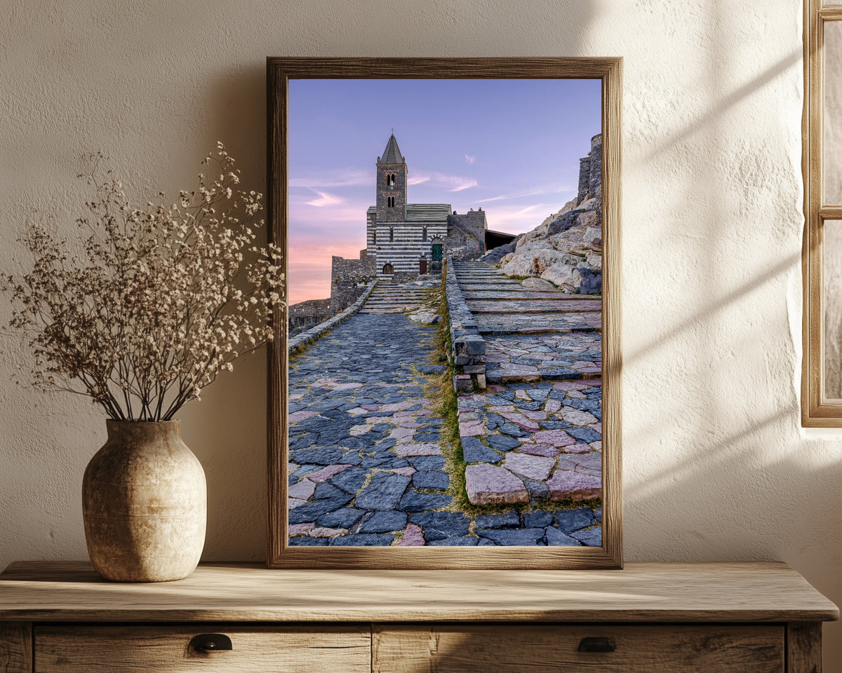 Framed art print of Porto Venere by Pablo Meilán Campagnale, in a dark wood frame leaning on a rustic console beside dried flowers