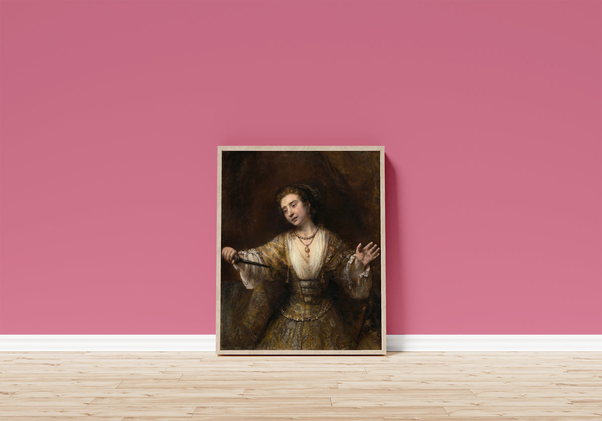 Framed art print of Lucretia by Rembrandt van Rijn, in a light wood frame leaning on a pink wall above a wooden floor