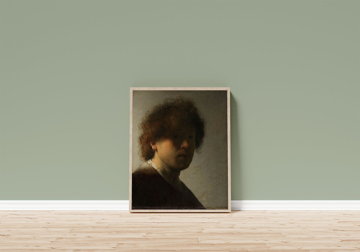 Framed art print of Self-portrait by Rembrandt van Rijn, in a light wood frame leaning on a sage green wall above a wooden floor