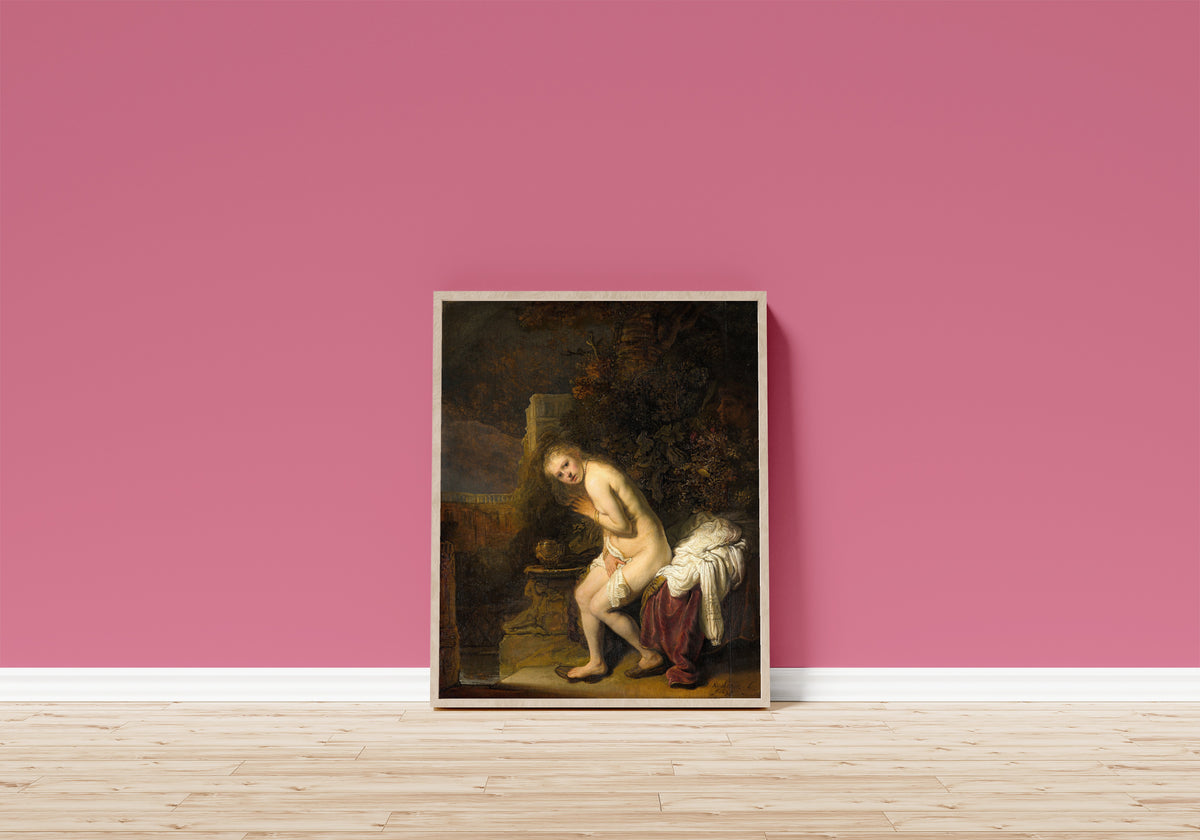 Framed art print of Susanna by Rembrandt van Rijn, in a light wood frame leaning on a pink wall above a wooden floor