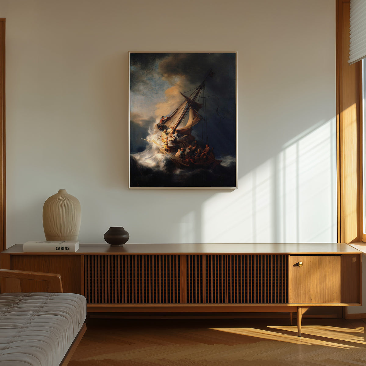 Framed art print of The Storm on the Sea of Galilee by Rembrandt van Rijn, in a thin light frame on a sunlit wall above a wooden sideboard
