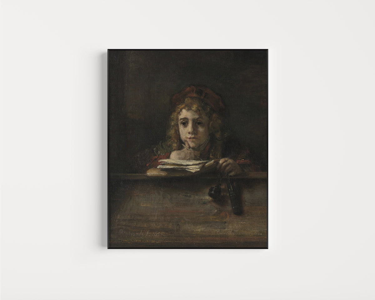 Framed art print of Titus at His Desk by Rembrandt van Rijn, in a slim black frame on a plain white wall