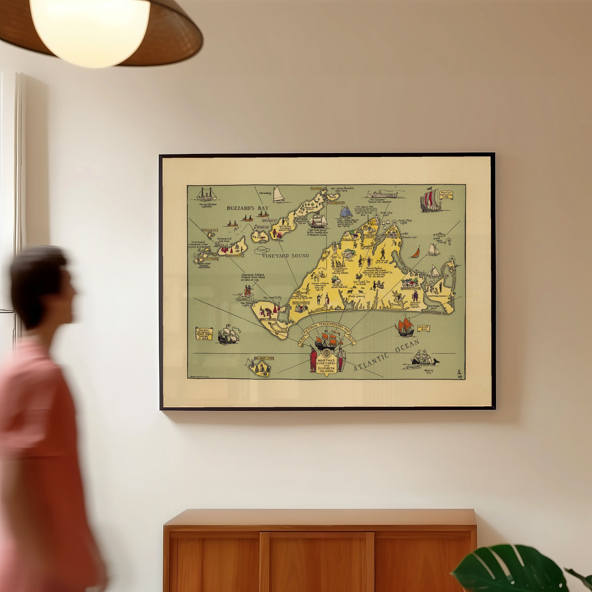Framed art print of Pictorial Tercentenary Map of Martha's Vineyard and… by Reynold's Printing Co., in a slim black frame on a warm wall in a sunlit room