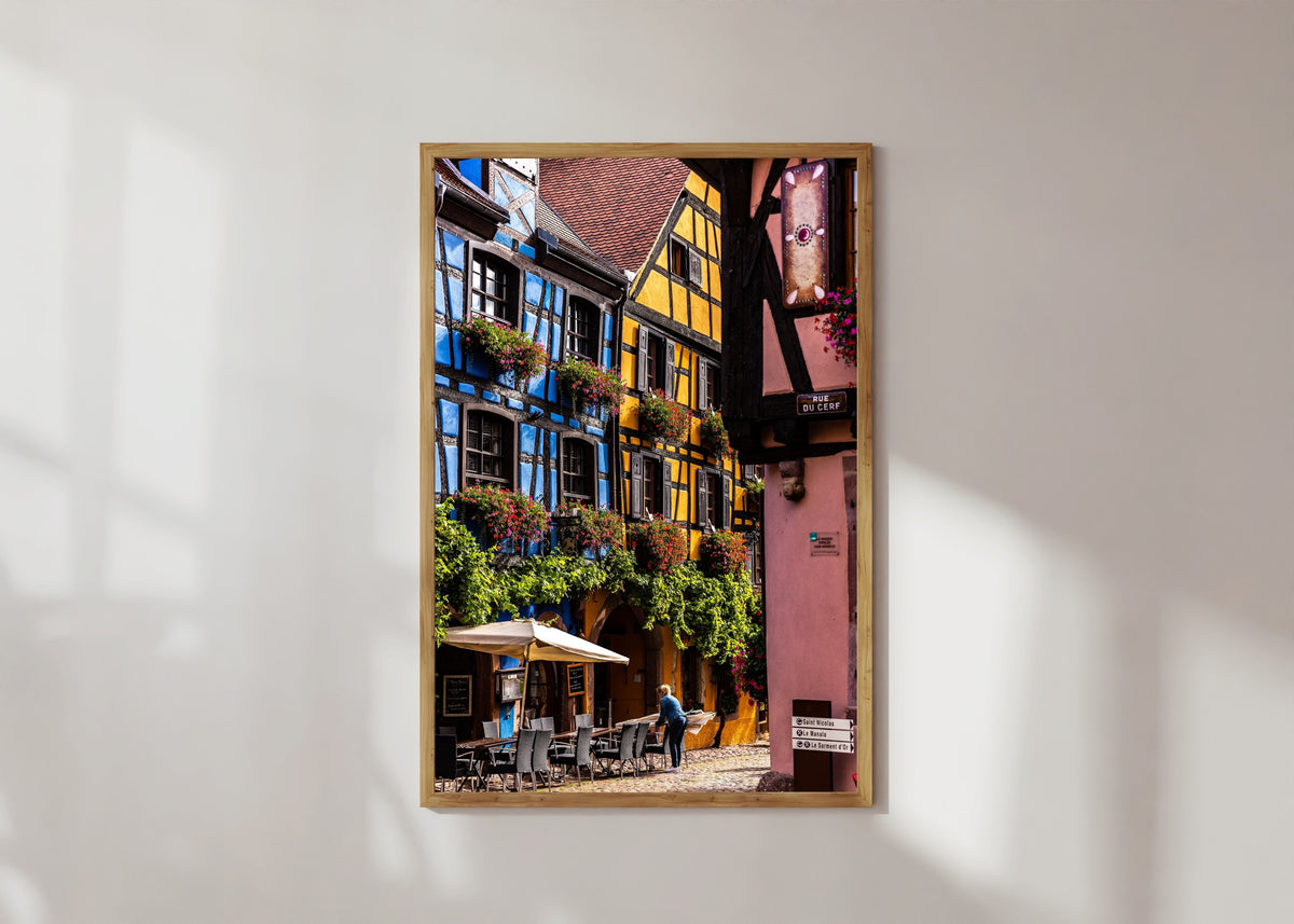 Framed art print of Riquewihr (Alsace) by Daniela Faust, in a light wood frame on a sunlit white wall