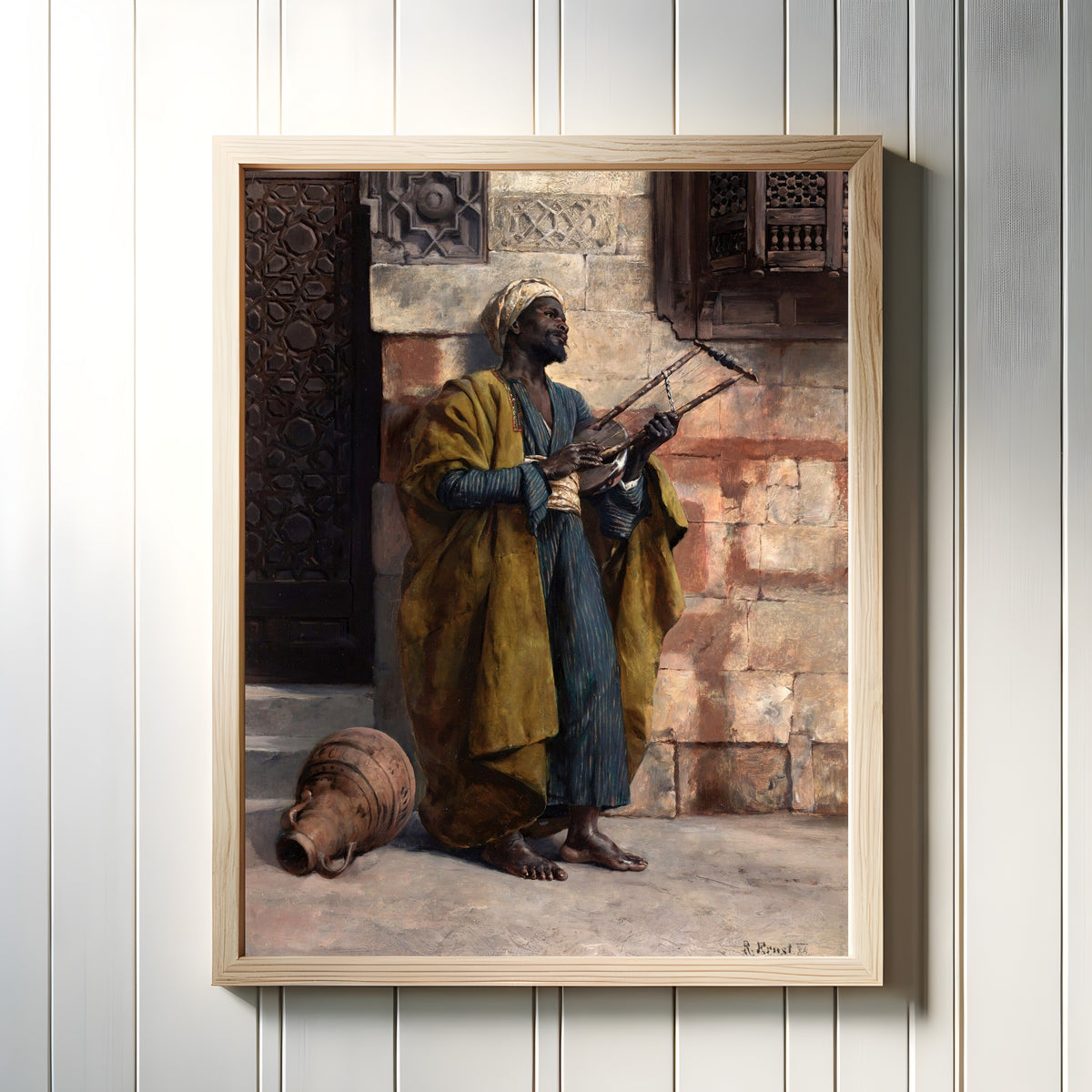 Framed art print of The Musician by Rudolf Ernst, in a light wood frame on a white panelled wall