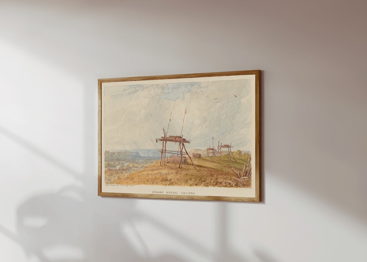Framed art print of Indian Burial Ground by Seth Eastman, in a light wood frame on a sunlit white wall, seen at a slight angle