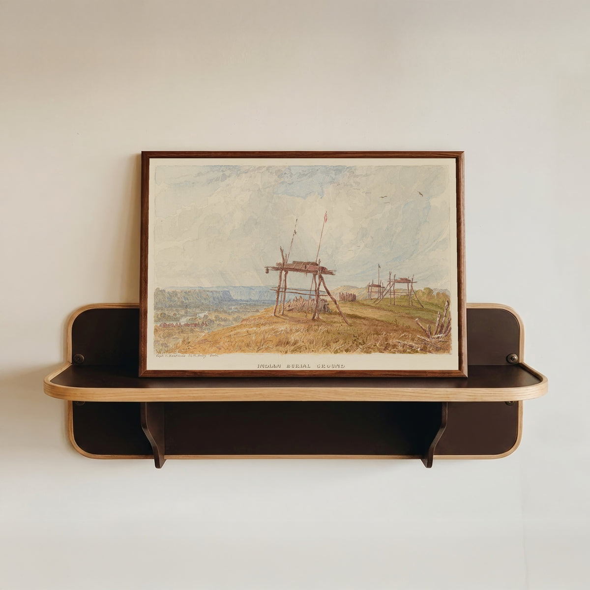 Framed art print of Indian Burial Ground by Seth Eastman, in a dark wood frame resting on a wall shelf