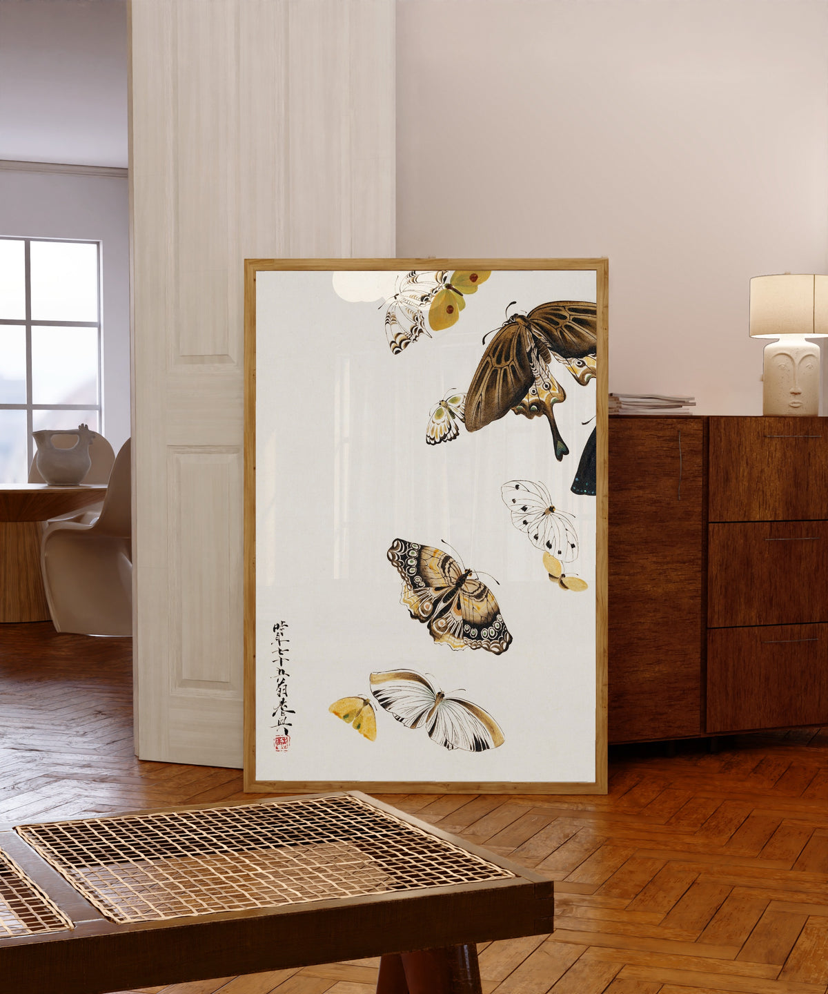 Framed art print of Butterflies by Shibata Zeshin, in a light wood frame leaning in a warm room with a parquet floor