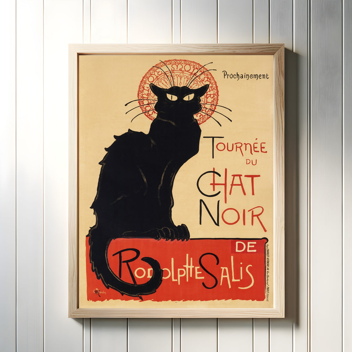 Framed art print of Chat Noir by Théophile Steinlen, in a light wood frame on a white panelled wall