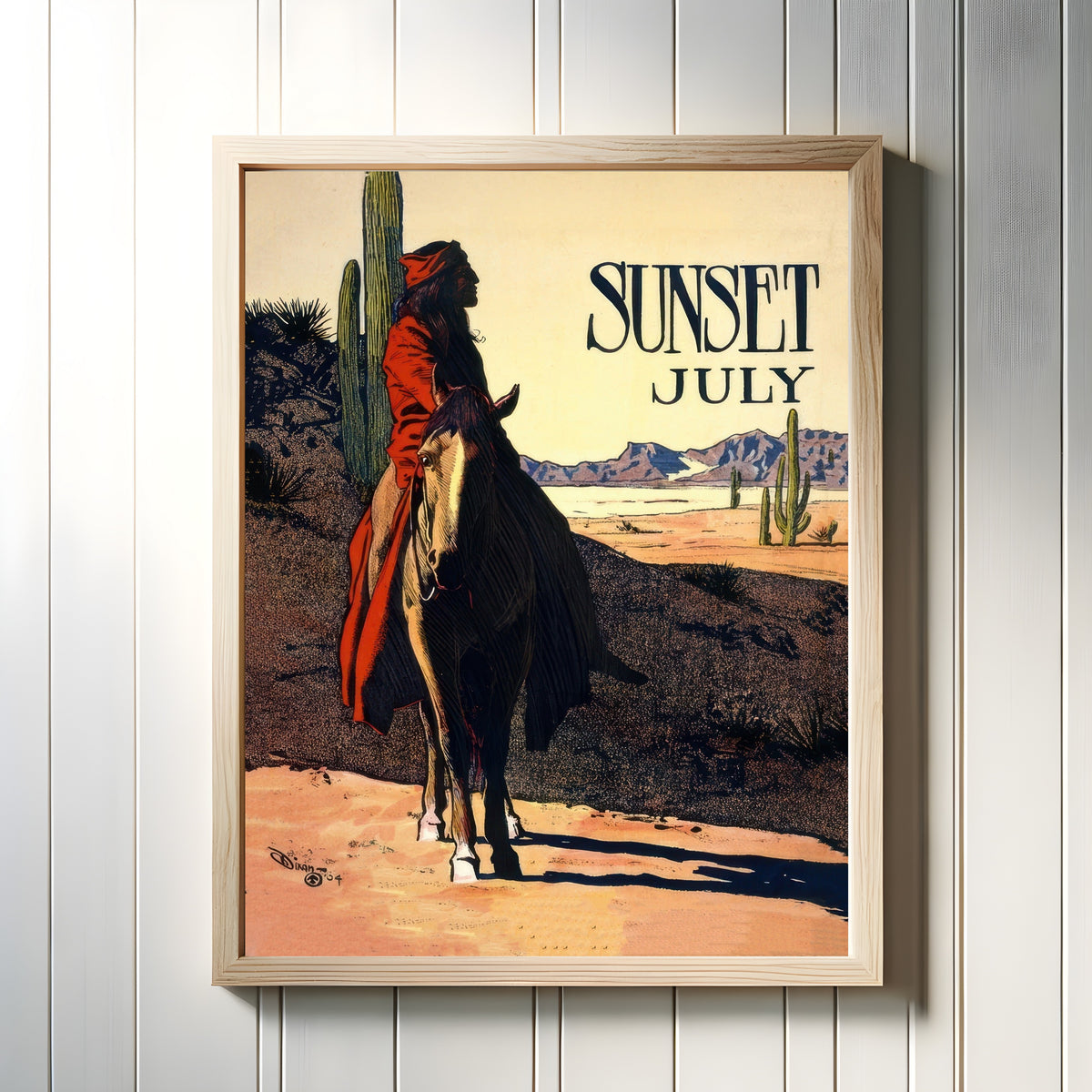 Framed art print of Sunset Magazine (July 1904) by Maynard Dixon, in a light wood frame on a white panelled wall
