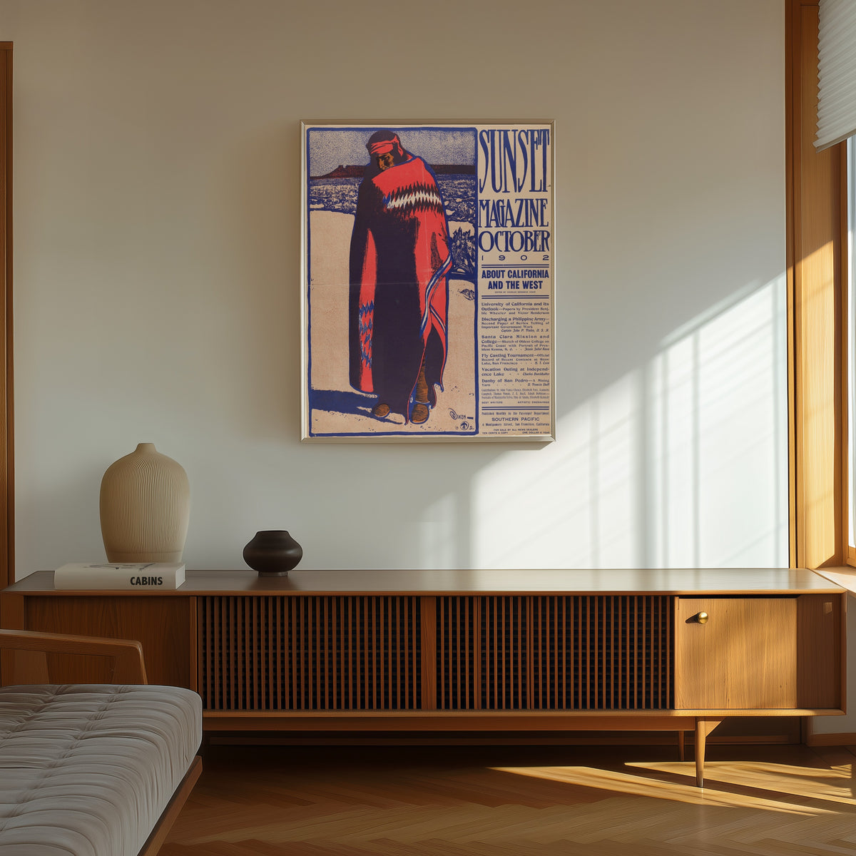 Framed art print of Sunset Magazine (October 1902) by Maynard Dixon, in a thin light frame on a sunlit wall above a wooden sideboard