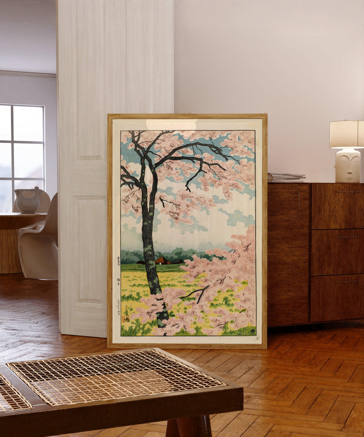 Framed art print of Nekata (Cherry Blossoms) by Takahashi Shotei, in a light wood frame leaning in a warm room with a parquet floor