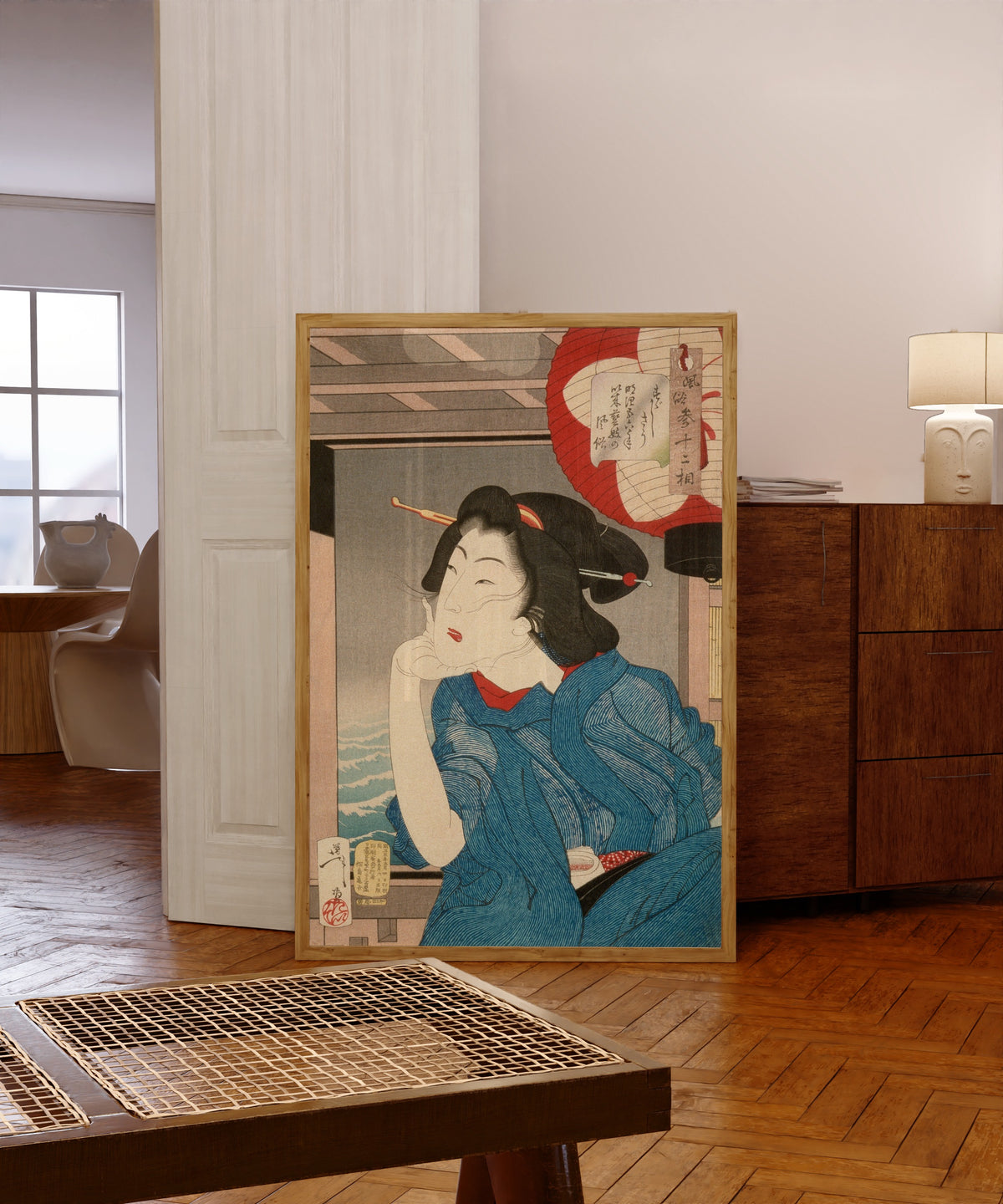 Framed art print of A Geisha of the Mid-1870s Seated in a Boat by Tsukioka Yoshitoshi, in a light wood frame leaning in a warm room with a parquet floor