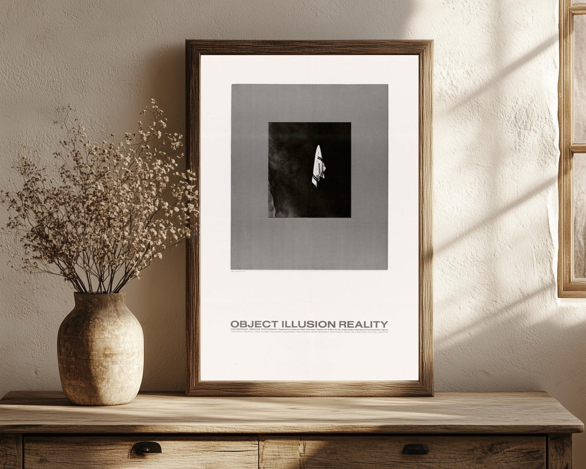 Framed art print of Object, Illusion, Reality by USIA, in a dark wood frame leaning on a rustic console beside dried flowers