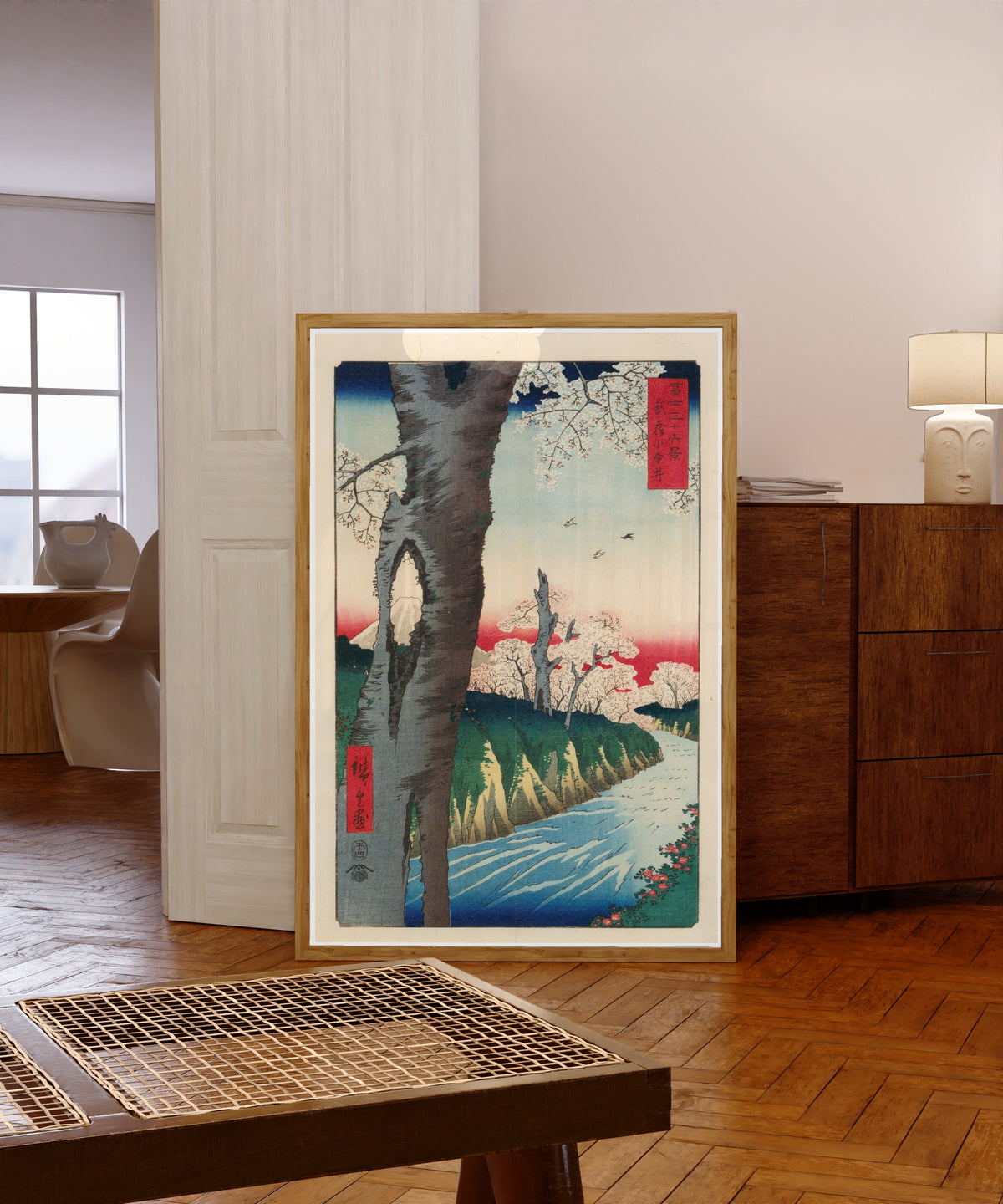 Framed art print of Koganei in Musashi Province by Utagawa Hiroshige, in a light wood frame leaning in a warm room with a parquet floor
