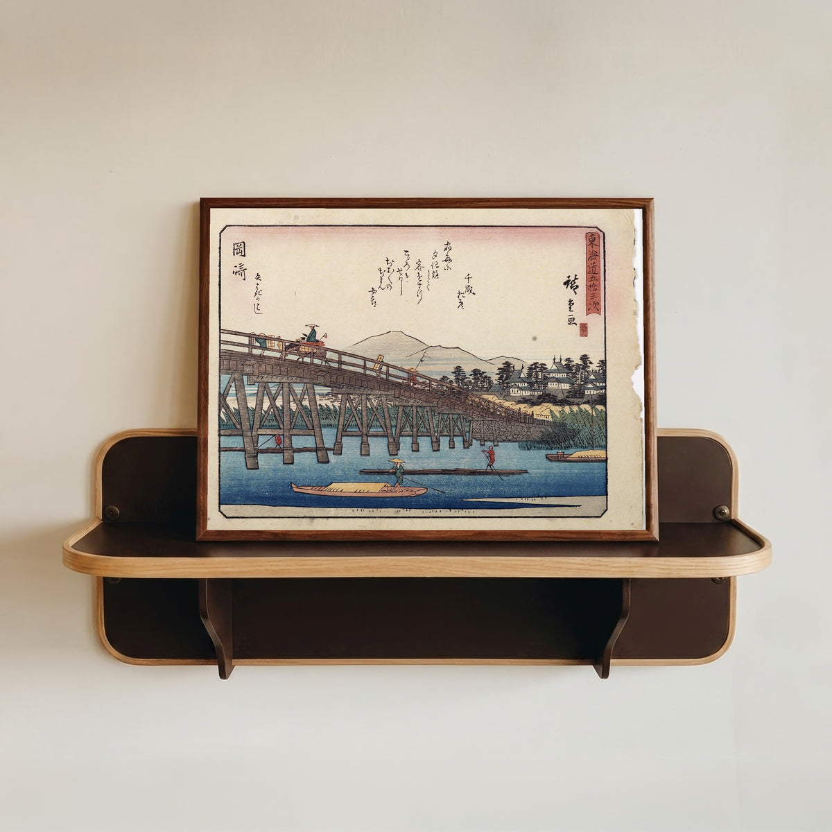 Framed art print of Kyōka Tōkaidō: Okazaki, Yahagi Bridge by Utagawa Hiroshige, in a dark wood frame resting on a wall shelf